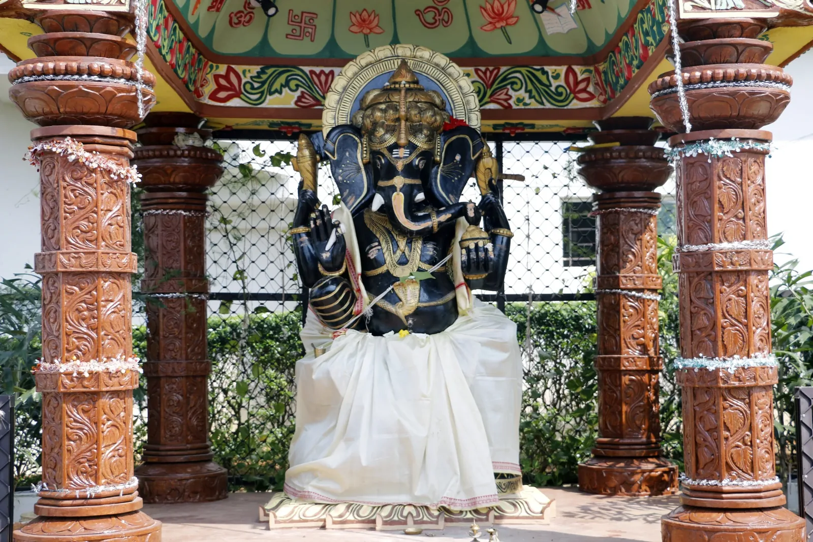 A Ganesha idol framed by carved wooden pillars on the school campus