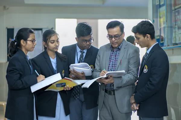 A teacher reviewing work with senior students in the school corridor.