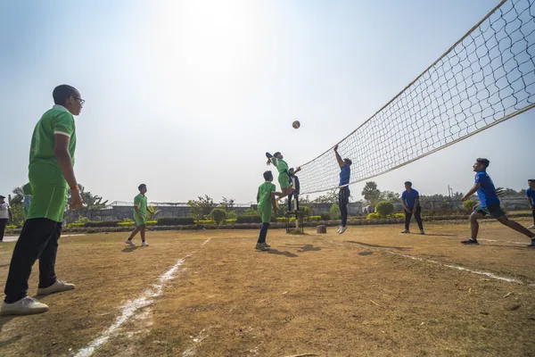 Volleyball match on the school court in green and blue jerseys.