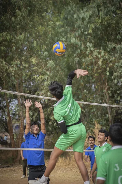 Student spiking a volleyball over the net in a blue JPS jersey.